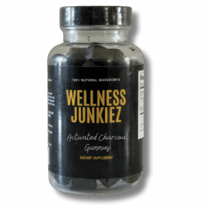 A clear bottle filled with dark Wellness Junkiez Activated Charcoal gummy supplements.