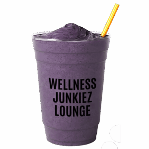 Slim Dealer mixed berry smoothie in a clear cup with Wellness Junkiez Lounge logo, yellow straw, and fresh blueberries, raspberries, strawberries, and blackberries on a white background.