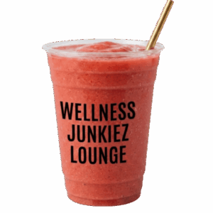 Mango strawberry The Glow Dealer smoothie in a clear cup with Wellness Junkiez Lounge logo, gold straw, fresh whole strawberries, diced mango, and microgreens on a white background.
